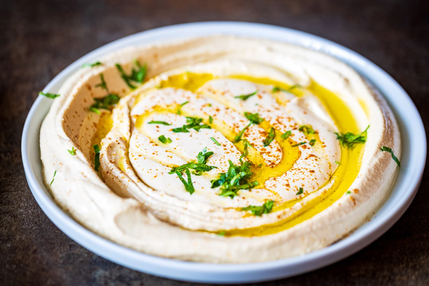 חומוס חלק בצלחת עם שמן זית, פפריקה ופטרוזיליה
